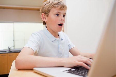 face to internet technology - Surprised boy using a notebook in a kitchen Photographie de stock - Aubaine LD & Abonnement, Code: 400-05749522