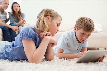 simsearch:400-05749633,k - Siblings using a tablet computer with their parents on the background in a living room Stock Photo - Budget Royalty-Free & Subscription, Code: 400-05749634