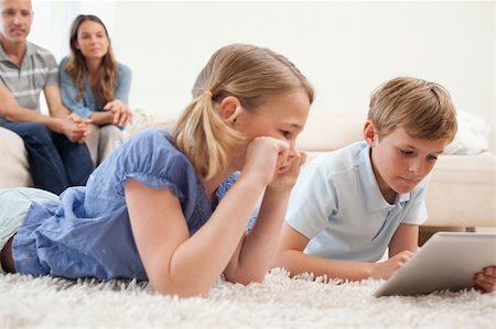 simsearch:400-05749633,k - Children using a tablet computer with their parents on the background in a living room Stock Photo - Budget Royalty-Free & Subscription, Code: 400-05749635