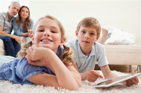 simsearch:400-05749633,k - Happy children using a tablet computer with their parents on the background in a living room Stock Photo - Budget Royalty-Free & Subscription, Code: 400-05749636