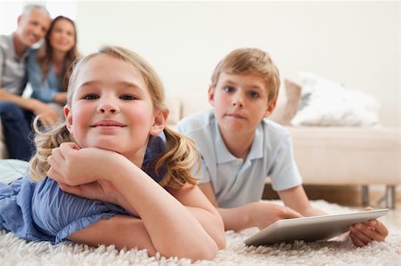 simsearch:400-05749633,k - Happy siblings using a tablet computer with their parents on the background in a living room Stock Photo - Budget Royalty-Free & Subscription, Code: 400-05749637