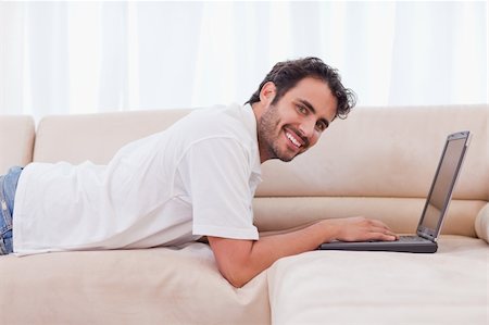 simsearch:400-04412244,k - Smiling man using a notebook in his living room Stock Photo - Budget Royalty-Free & Subscription, Code: 400-05741532