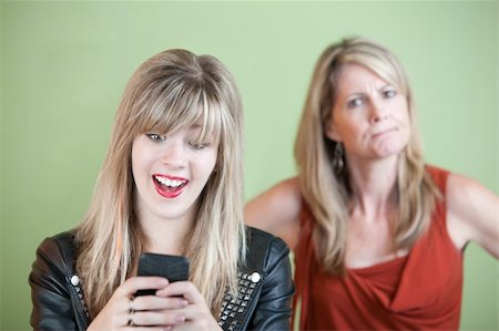 simsearch:400-05918419,k - Angry woman behind excited teen on mobile phone Stock Photo - Budget Royalty-Free & Subscription, Code: 400-05754654