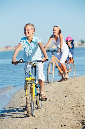 simsearch:400-05755734,k - Cute girl with her mother and brother ride bikes along the beach. Focus on girl. Vertical view Photographie de stock - Aubaine LD & Abonnement, Code: 400-05875951