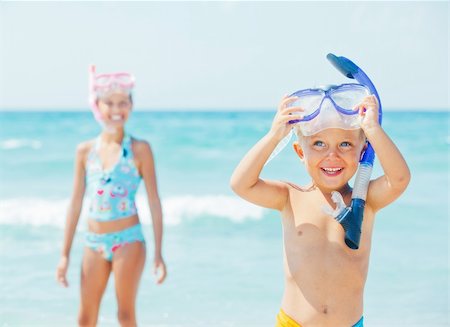 Happy young boy with snorkeling equipment on sandy tropical beach, his sister background. Stock Photo - Budget Royalty-Free & Subscription, Code: 400-05877577