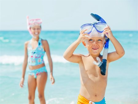Happy young boy with snorkeling equipment on sandy tropical beach, his sister background. Stock Photo - Budget Royalty-Free & Subscription, Code: 400-05877593