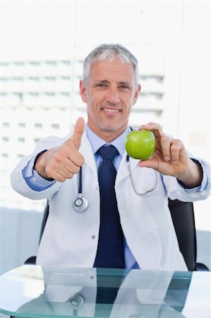Portrait of a doctor showing an apple with the thumb up in his office Stock Photo - Budget Royalty-Free & Subscription, Code: 400-05892411