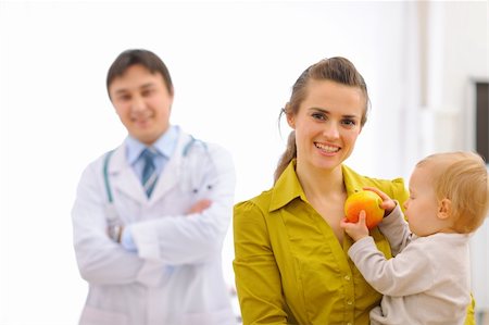 Portrait of mother with baby holding apple and doctor in background Stock Photo - Budget Royalty-Free & Subscription, Code: 400-05908550