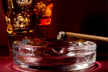 simsearch:400-05207678,k - Close-up selective focus of a burning cigar with a glass of whiskey in the background. Stock Photo - Budget Royalty-Free & Subscription, Code: 400-06079519