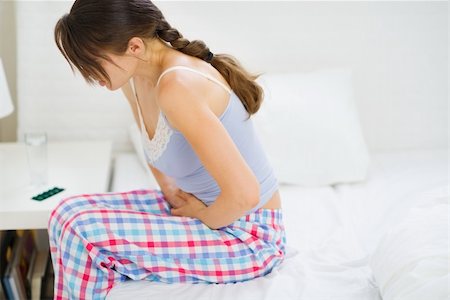 simsearch:400-07343634,k - Girl with stomach ache sitting on bed Stock Photo - Budget Royalty-Free & Subscription, Code: 400-06106823