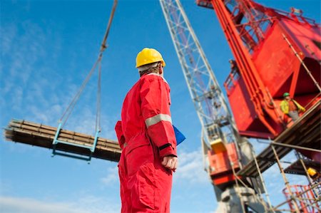 Construction operator looking at a crane carrying scaffolding materials to a super sized structure at a building site Stock Photo - Budget Royalty-Free & Subscription, Code: 400-06137766