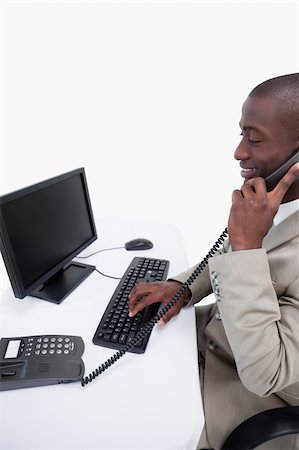 simsearch:859-06710917,k - Side view of a male secretary answering the phone while using a computer against a white background Stock Photo - Budget Royalty-Free & Subscription, Code: 400-06627041