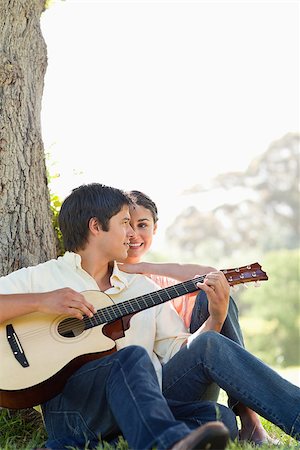 picture of the blue playing a instruments - Man sitting against the trunk of a tree while playing a guitar as his friend watches him Stock Photo - Budget Royalty-Free & Subscription, Code: 400-06635932