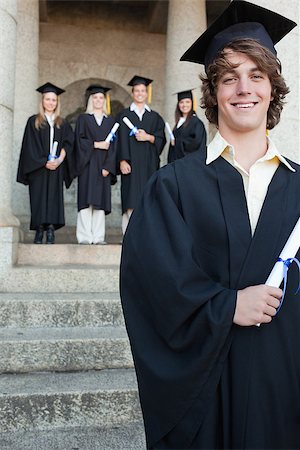 simsearch:400-06688304,k - Close-up of a handsome graduate smiling with her friends in background in front of the university Photographie de stock - Aubaine LD & Abonnement, Code: 400-06688426