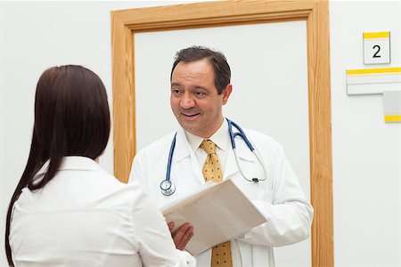 Smiling doctor holding a file while talking to a woman in a hallway Stock Photo - Budget Royalty-Free & Subscription, Code: 400-06734138