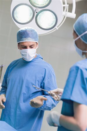 simsearch:400-06734297,k - Nurse giving surgical scissors to a doctor in operating theater Stock Photo - Budget Royalty-Free & Subscription, Code: 400-06734306