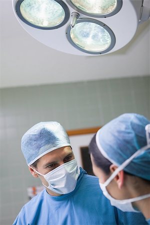 simsearch:400-06734297,k - Doctor looking at a nurse below the light in operating theater Stock Photo - Budget Royalty-Free & Subscription, Code: 400-06734519