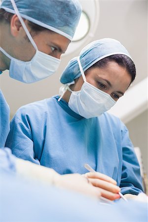 simsearch:400-06734297,k - Doctor looking at another doctor while operating in operating theater Stock Photo - Budget Royalty-Free & Subscription, Code: 400-06734608