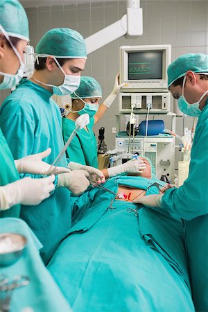Side view of a surgical team next to a patient in an operating theatre Stock Photo - Budget Royalty-Free & Subscription, Code: 400-06735474