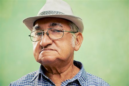 simsearch:400-06142278,k - people and emotions, portrait of serious senior hispanic man with glasses and hat looking at camera against green background Stock Photo - Budget Royalty-Free & Subscription, Code: 400-06737720