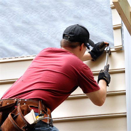 redoing - First time home buyer works to install siding on his new home.  He is hammering into place a sheet of siding.  He has on a red shirt and is holding hammer and nail. Stock Photo - Budget Royalty-Free & Subscription, Code: 400-06788534
