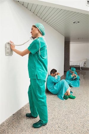 Surgeon using the phone in hospital corridor with two surgeons sitting on floor Stock Photo - Budget Royalty-Free & Subscription, Code: 400-06799544