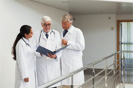 Three doctors talking in the corridor looking at patient files Stock Photo - Budget Royalty-Free & Subscription, Code: 400-06799672