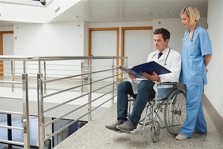 Doctor sitting in wheelchair examining notes with nurse in hospital corridor Stock Photo - Budget Royalty-Free & Subscription, Code: 400-06799813
