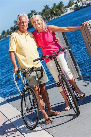 Happy senior man and woman couple together cycling on bicycles with bright clear blue sky by a river or sea Stock Photo - Budget Royalty-Free & Subscription, Code: 400-06856550