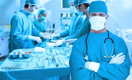 Surgeon standing with arms crossed with surgery going on behind him Stock Photo - Budget Royalty-Free & Subscription, Code: 400-06875885