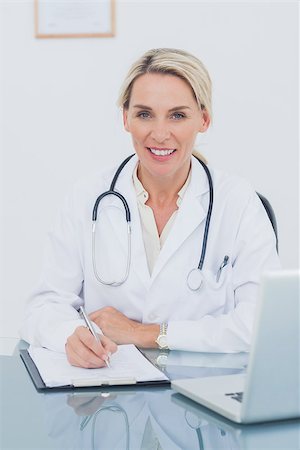 Portrait of an attractive doctor posing in her office while writing on a clipboard Stock Photo - Budget Royalty-Free & Subscription, Code: 400-06884189