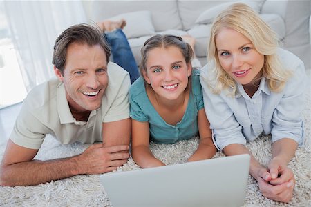 Portrait of parents and daughter using a laptop lying on a carpet Stock Photo - Budget Royalty-Free & Subscription, Code: 400-06887734