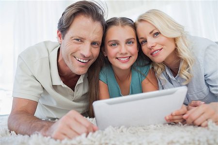 Portrait of a girl and her parents using a tablet lying on a carpet Stock Photo - Budget Royalty-Free & Subscription, Code: 400-06887740