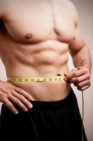 fat man exercising - Fit man measuring his waist after a workout in the gym, in a dark brown background Stock Photo - Budget Royalty-Free & Subscription, Code: 400-06914118