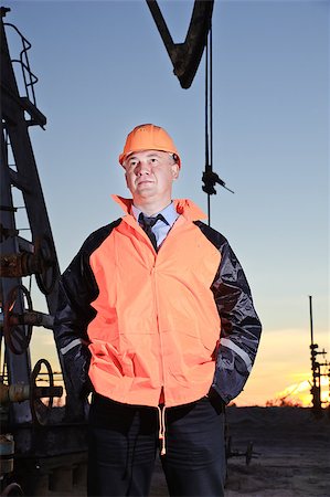 Worker in orange uniform and helmet on of background the pump jack and sunset sky. Severe. Hands in pockets. Stock Photo - Budget Royalty-Free & Subscription, Code: 400-07040599