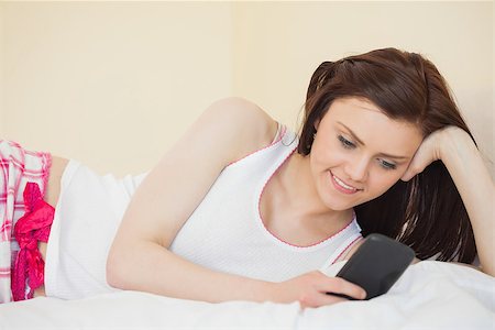 Content brunette looking and using her phone lying on a bed in a bedroom Stock Photo - Budget Royalty-Free & Subscription, Code: 400-07059105