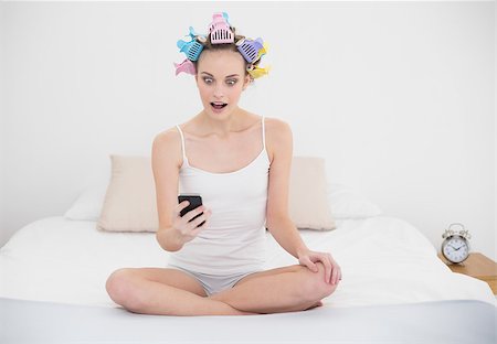 simsearch:400-07129766,k - Astonished natural brown haired woman in hair curlers looking at her mobile phone in bright bedroom Stock Photo - Budget Royalty-Free & Subscription, Code: 400-07129748
