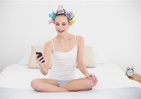 simsearch:400-07129766,k - Cheerful natural brown haired woman in hair curlers looking at her mobile phone in bright bedroom Stock Photo - Budget Royalty-Free & Subscription, Code: 400-07129749