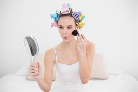 simsearch:400-07129766,k - Pouting natural brown haired woman in hair curlers applying powder on her face in bright bedroom Stock Photo - Budget Royalty-Free & Subscription, Code: 400-07129755