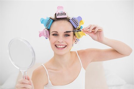 simsearch:400-07129766,k - Happy natural brown haired woman in hair curlers brushing her eyebrows in bright bedroom Stock Photo - Budget Royalty-Free & Subscription, Code: 400-07129759