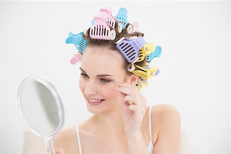 simsearch:400-07129766,k - Cute natural brown haired woman in hair curlers plucking her eyebrows in bright bedroom Stock Photo - Budget Royalty-Free & Subscription, Code: 400-07129764