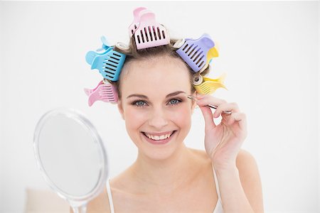 simsearch:400-07129766,k - Charming natural brown haired woman in hair curlers plucking her eyebrows in bright bedroom Stock Photo - Budget Royalty-Free & Subscription, Code: 400-07129765