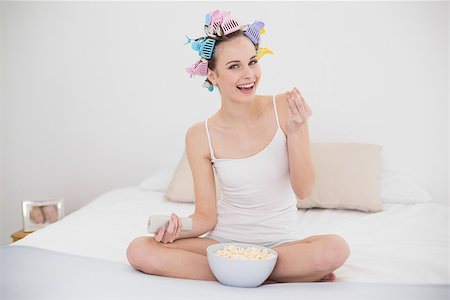simsearch:400-07129766,k - Happy natural brown haired woman in hair curlers watching tv while eating popcorn in bright bedroom Stock Photo - Budget Royalty-Free & Subscription, Code: 400-07129789