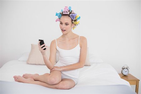 simsearch:400-07129766,k - Amazed natural brown haired woman in hair curlers looking at her mobile phone in bright bedroom Stock Photo - Budget Royalty-Free & Subscription, Code: 400-07129798