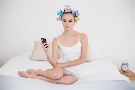 simsearch:400-07129766,k - Frowning natural brown haired woman in hair curlers looking at her mobile phone in bright bedroom Stock Photo - Budget Royalty-Free & Subscription, Code: 400-07129800