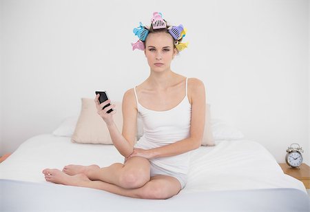 simsearch:400-07129766,k - Frowning natural brown haired woman in hair curlers holding a mobile phone in bright bedroom Stock Photo - Budget Royalty-Free & Subscription, Code: 400-07129801