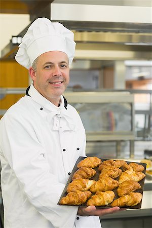 Baker showing some croissants on a baking tray smiling at the camera Stock Photo - Budget Royalty-Free & Subscription, Code: 400-07140079