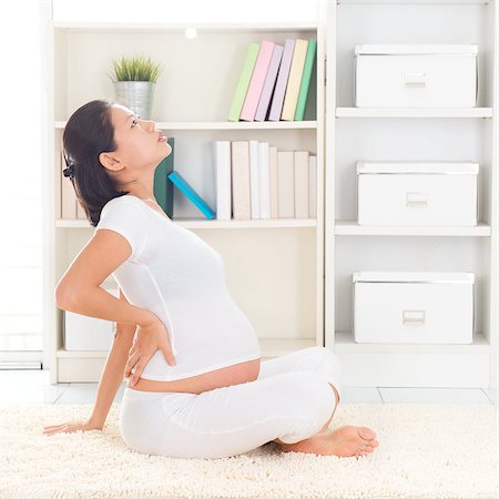 Back pain. Eight months pregnant Asian woman holding her back while sitting on a floor at home. Stock Photo - Budget Royalty-Free & Subscription, Code: 400-07167248