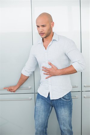 sad bald man - Casual young man with stomach pain standing against wardrobe at home Stock Photo - Budget Royalty-Free & Subscription, Code: 400-07177454