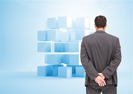 Composite image of businessman standing with hands behind back looking at plastic blue cubes in the background Stock Photo - Budget Royalty-Free & Subscription, Code: 400-07180302